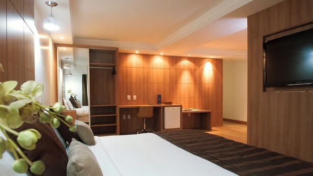 Habitación de hotel con cama, escritorio, televisor y una pequeña kitchenette.