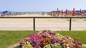 Egy strand, ahol sorokban állnak a napozóágyak és a napernyők, az előtérben egy virágágyás, és a háttérben tiszta az ég.