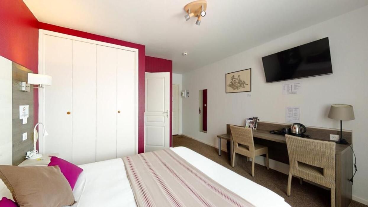 Habitación de hotel con cama, escritorio, silla, televisor y armario.