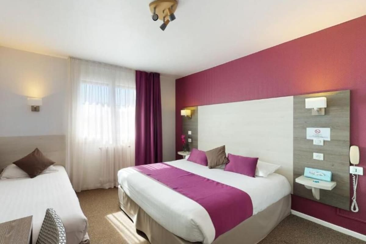 Une chambre d’hôtel avec deux lits, une table de chevet avec une lampe, un miroir et un téléphone fixé au mur.