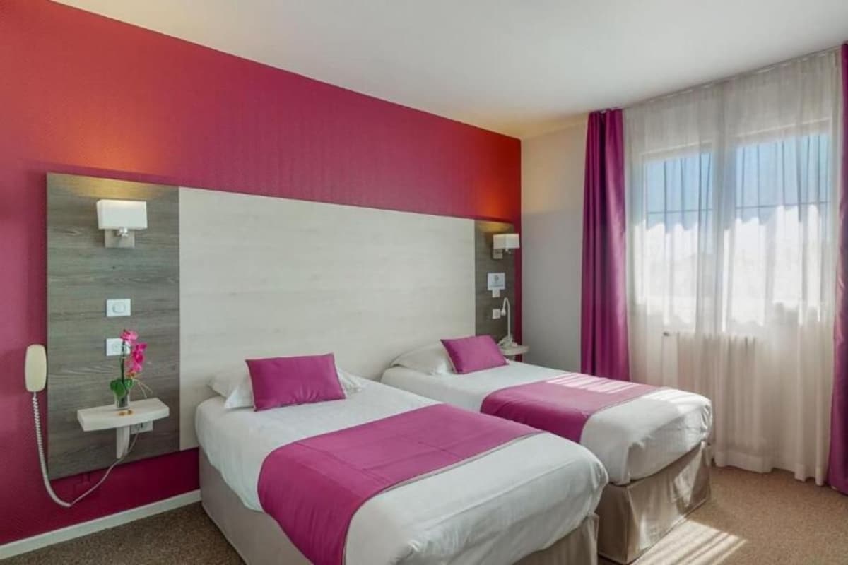 Une chambre d’hôtel avec deux lits, une table de chevet, une lampe, un téléphone et une fenêtre avec des rideaux.