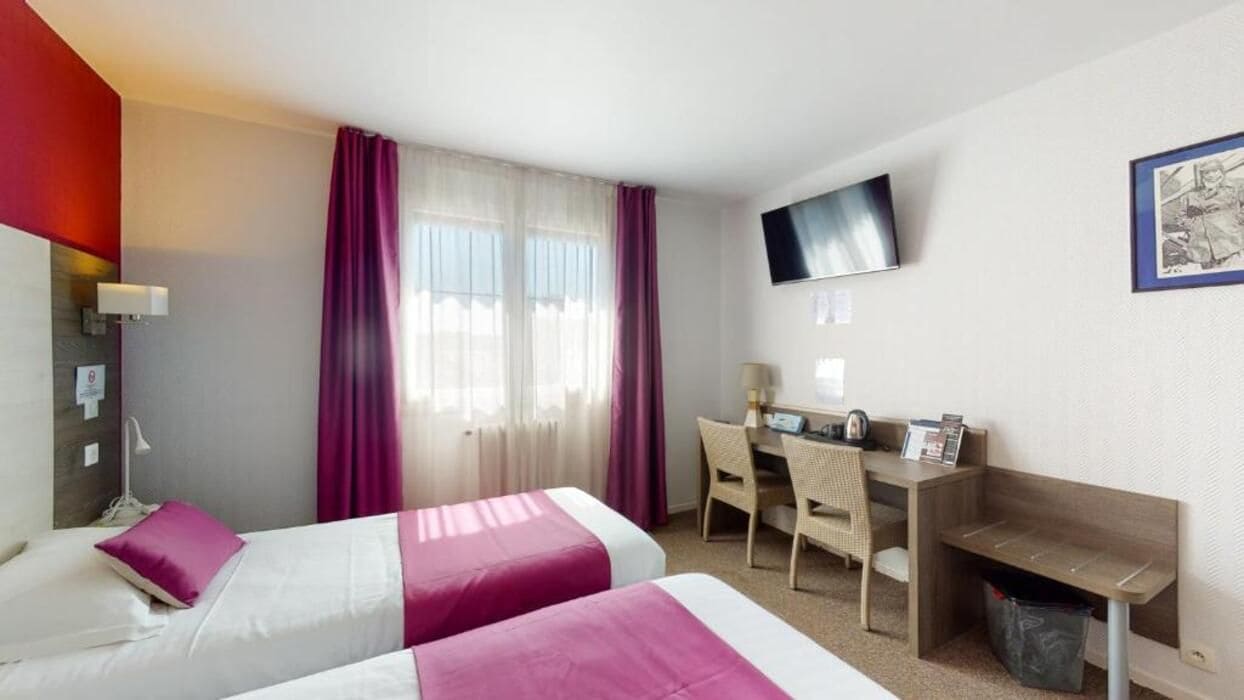 Habitación de hotel con dos camas, un escritorio, una silla, un televisor y un cesto de basura.