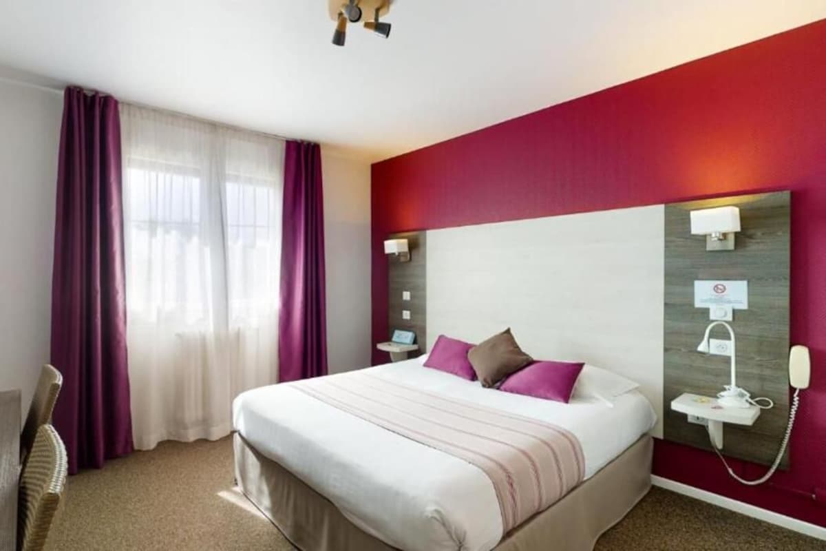 Une chambre d’hôtel avec un lit, un bureau, un téléphone et une fenêtre avec des rideaux.