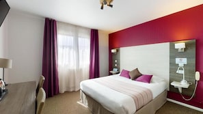 Une chambre d’hôtel avec un lit, un bureau, un téléphone et une fenêtre avec des rideaux.