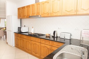Una cocina con armarios de madera, encimera negra, refrigerador blanco, microondas, tostadora y fregadero.