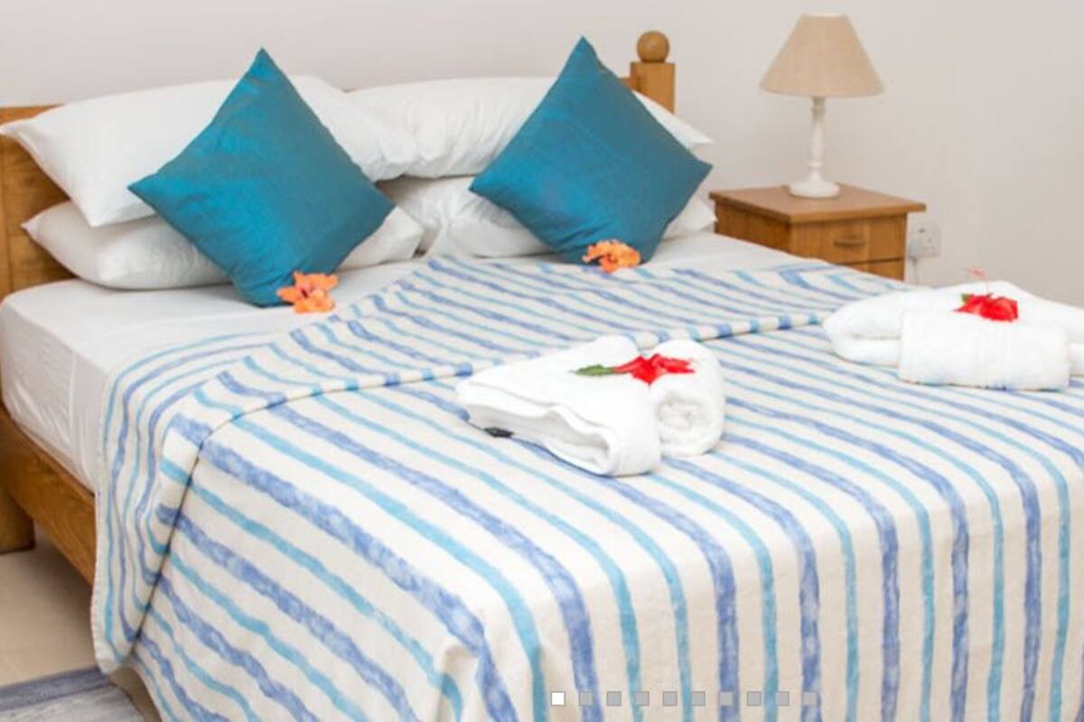 A neatly made bed with blue and white striped bedding, two blue pillows, and a wooden headboard.