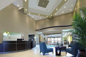 A hotel lobby with a reception desk, seating area, and a large potted plant.