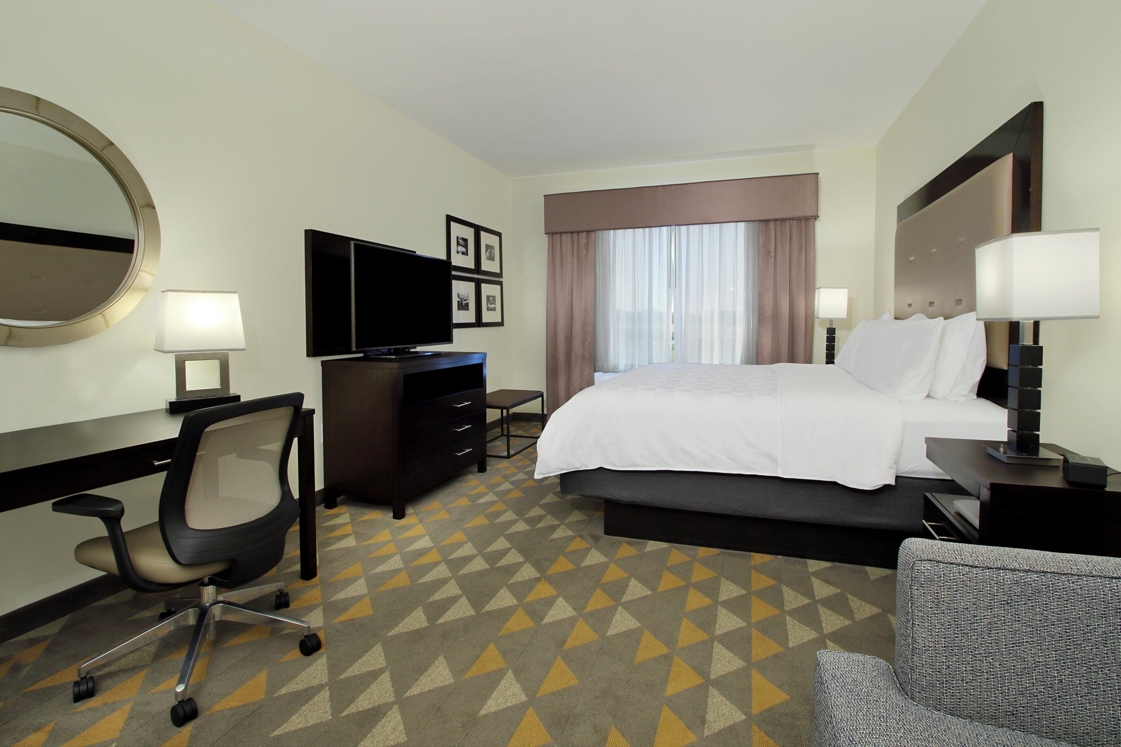 Une chambre d’hôtel équipée d’un lit, d’un bureau, d’une chaise, d’une télévision et d’une fenêtre avec des rideaux.