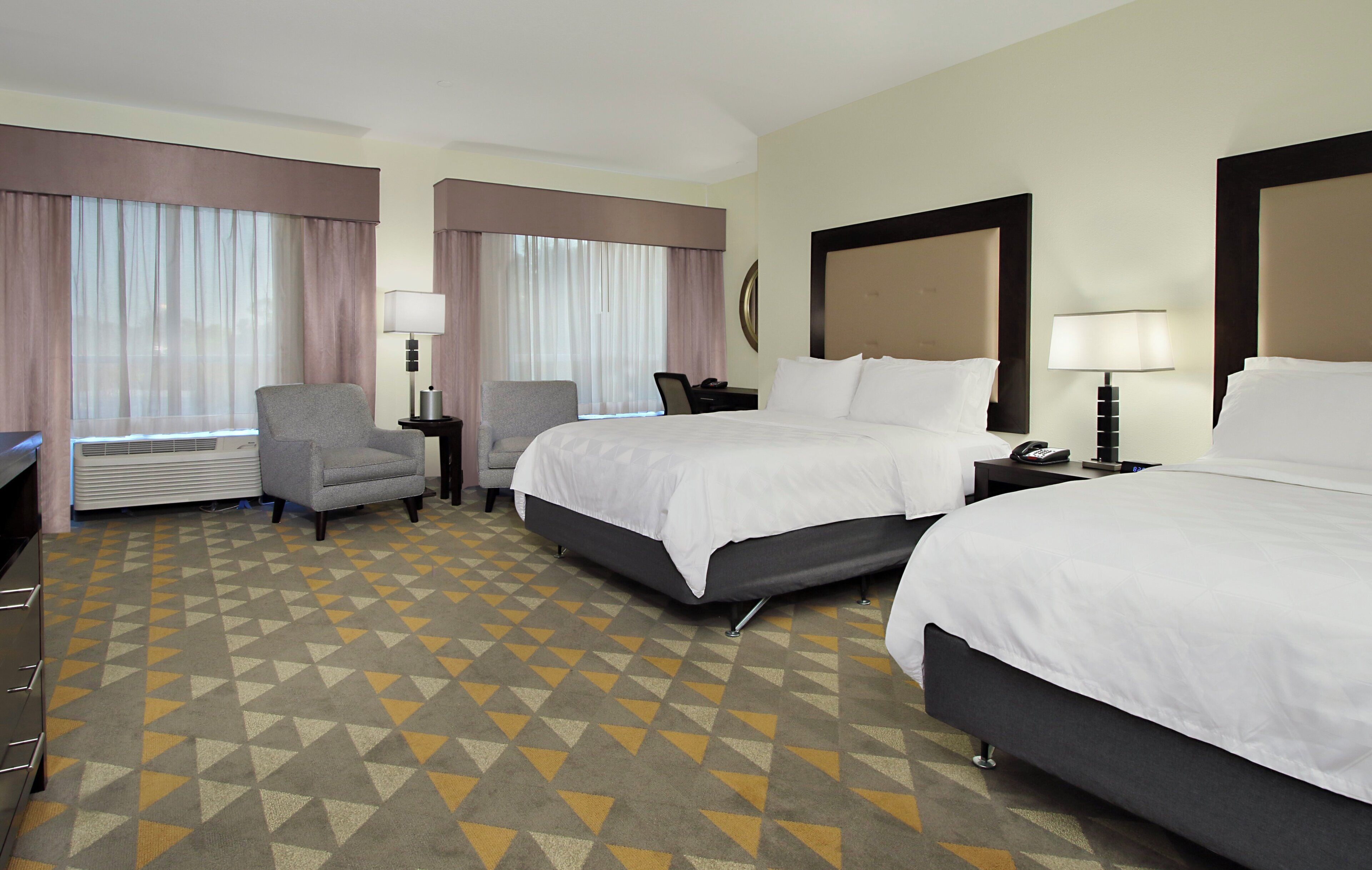 A hotel room with two beds, a desk, a chair, and a window with curtains.