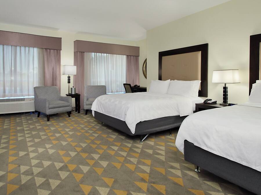A hotel room with two beds, a desk, a chair, and a window with curtains.