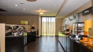 A modern hotel lobby with a bakery counter, a reception desk, and a large window with curtains. - Holiday Inn Hammond by IHG (Hammond)