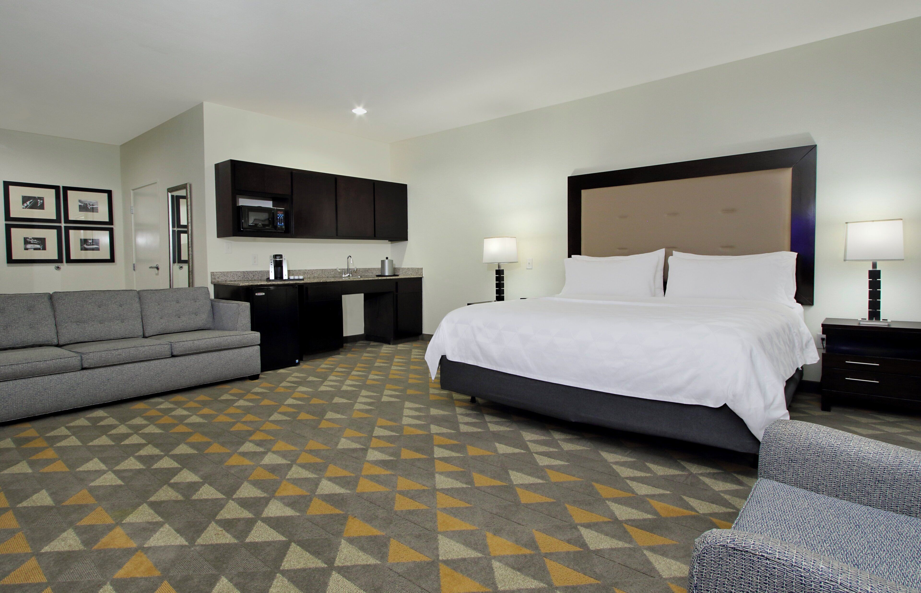 A hotel room with a bed, a sofa, a desk with a microwave, and a patterned floor.