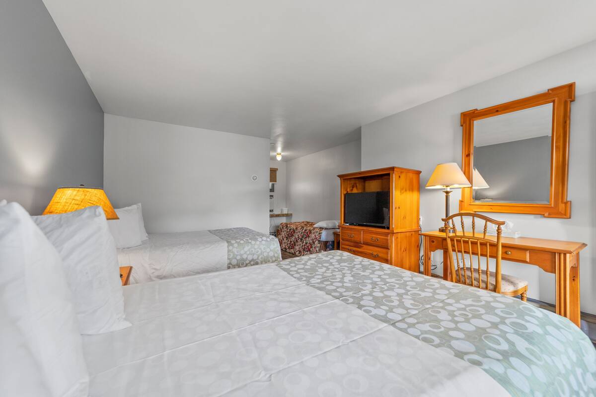 A hotel room with two beds, a wooden desk, a chair, a television, and a mirror.