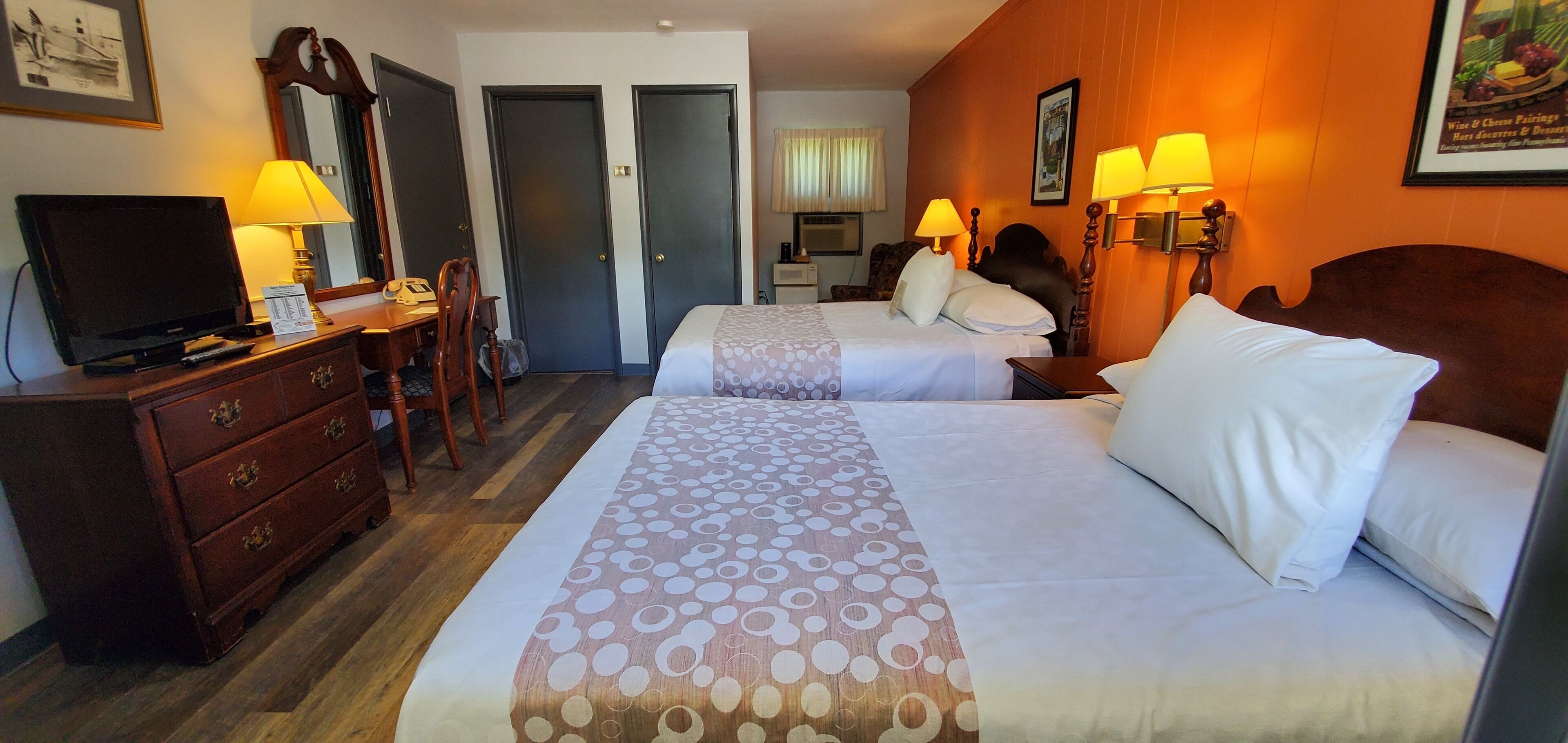 Quarto de hotel com duas camas, uma escrivaninha com luminária, televisão e cômoda.