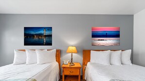 A hotel room with two beds, a nightstand with a lamp, and two framed pictures on the wall.
