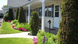 A house with a covered porch, a well-maintained lawn, and various flowering plants.