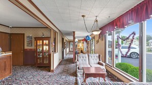 A hallway with patterned carpet, a seating area with striped sofas, and large windows with decorative garlands.
