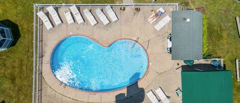 An aerial view of a swimming pool with a heart-shaped design, surrounded by lounge chairs and a fenced area.