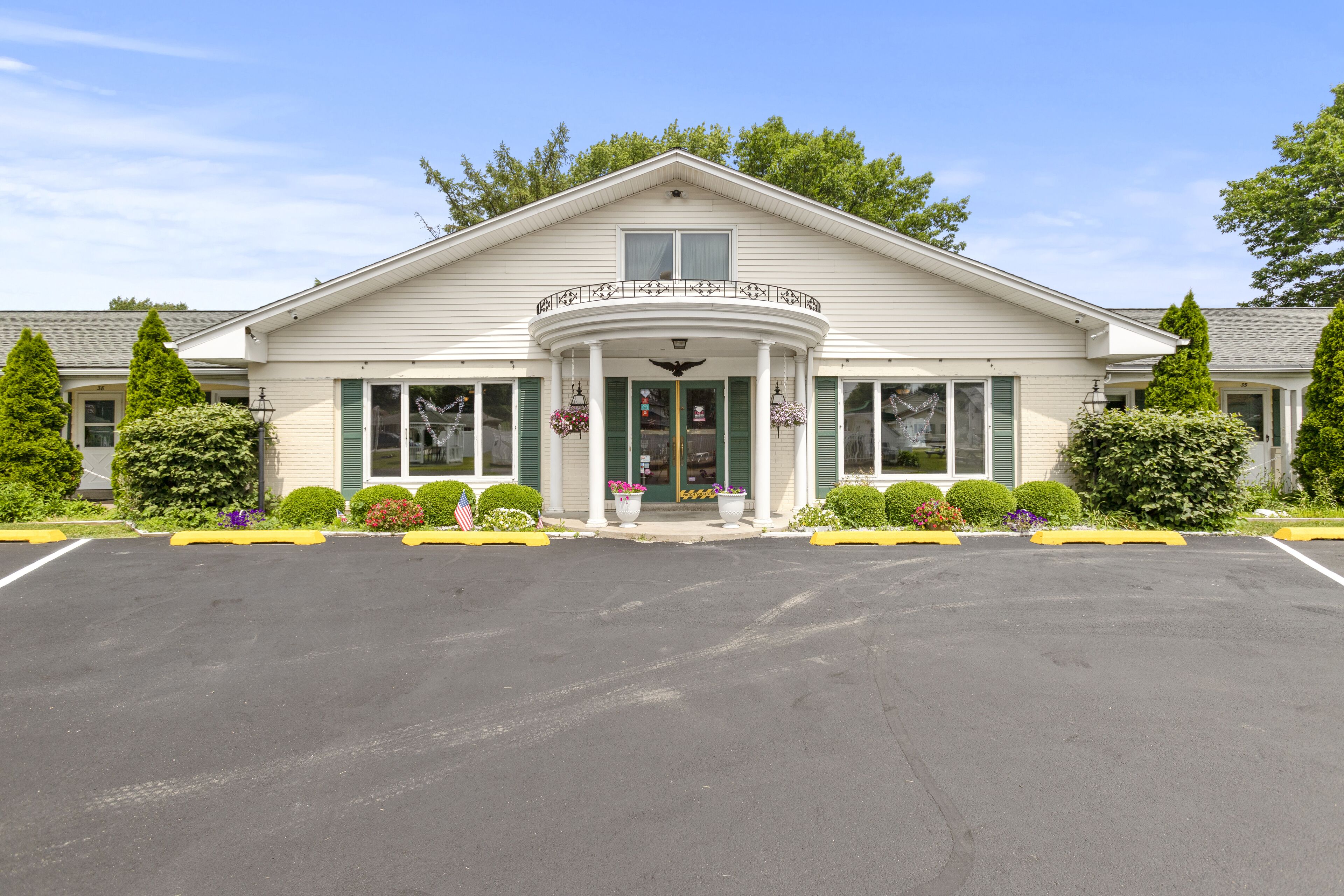 A two-story building with a central entrance, a balcony, and a parking lot in front.