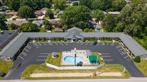 An aerial view of a large building with a parking lot, a swimming pool, and a gazebo.