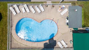 An aerial view of a swimming pool with a heart-shaped design, surrounded by lounge chairs and a fenced area.