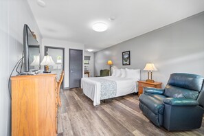 A hotel room with a bed, a desk, a chair, and a dresser.