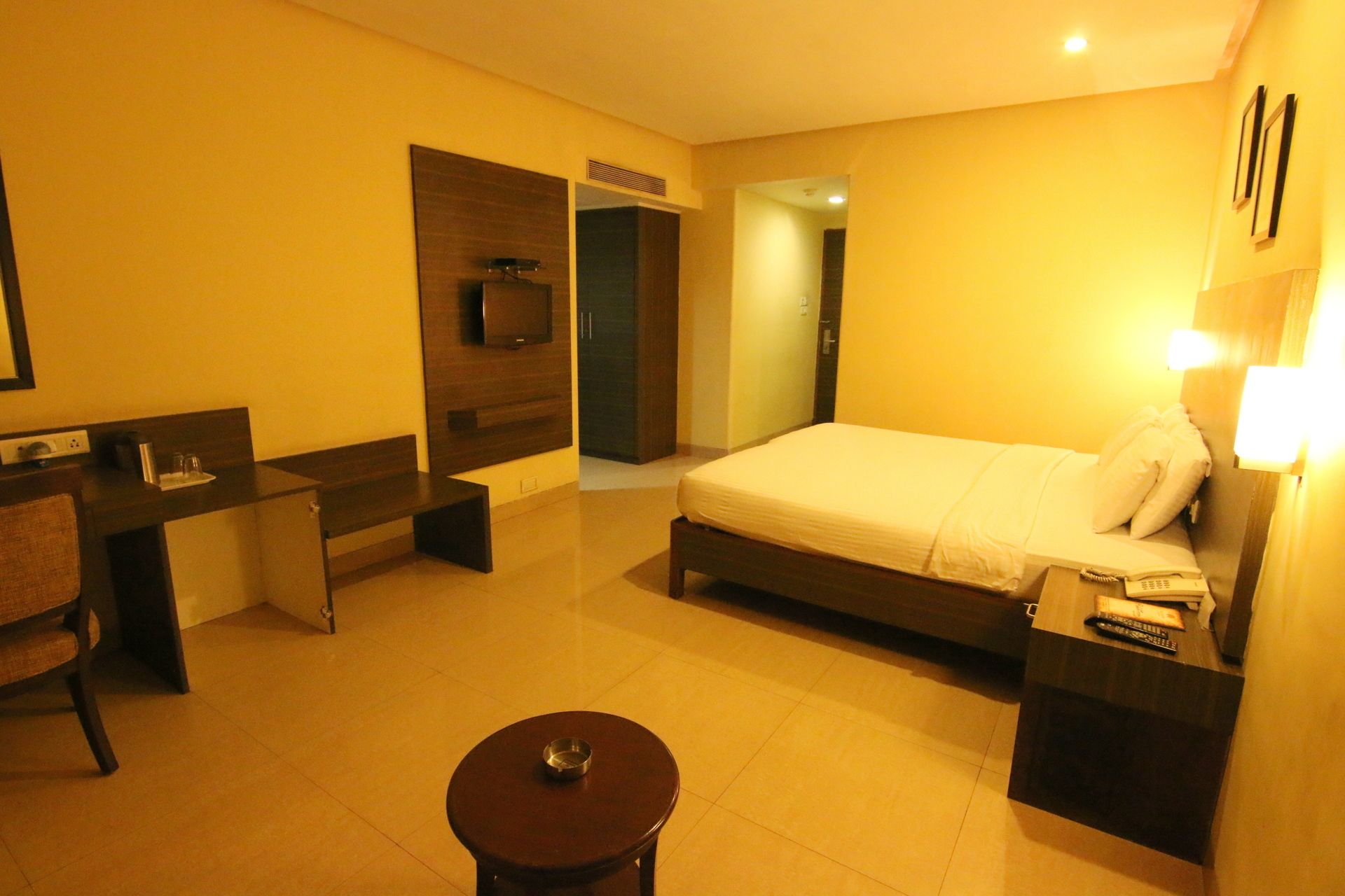 Habitació d'hotel amb llit, taula de nit, escriptori, cadira i taula rodona petita.