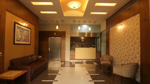 A hotel lobby with a reception desk, a sofa, a chair, and a patterned wall. - The Caliph Hotel (Mumbai)