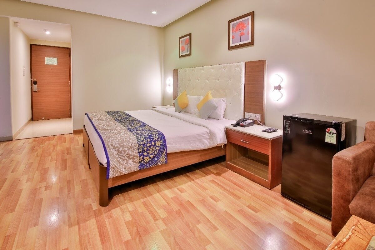 A hotel room with a bed, bedside table, refrigerator, and a door.