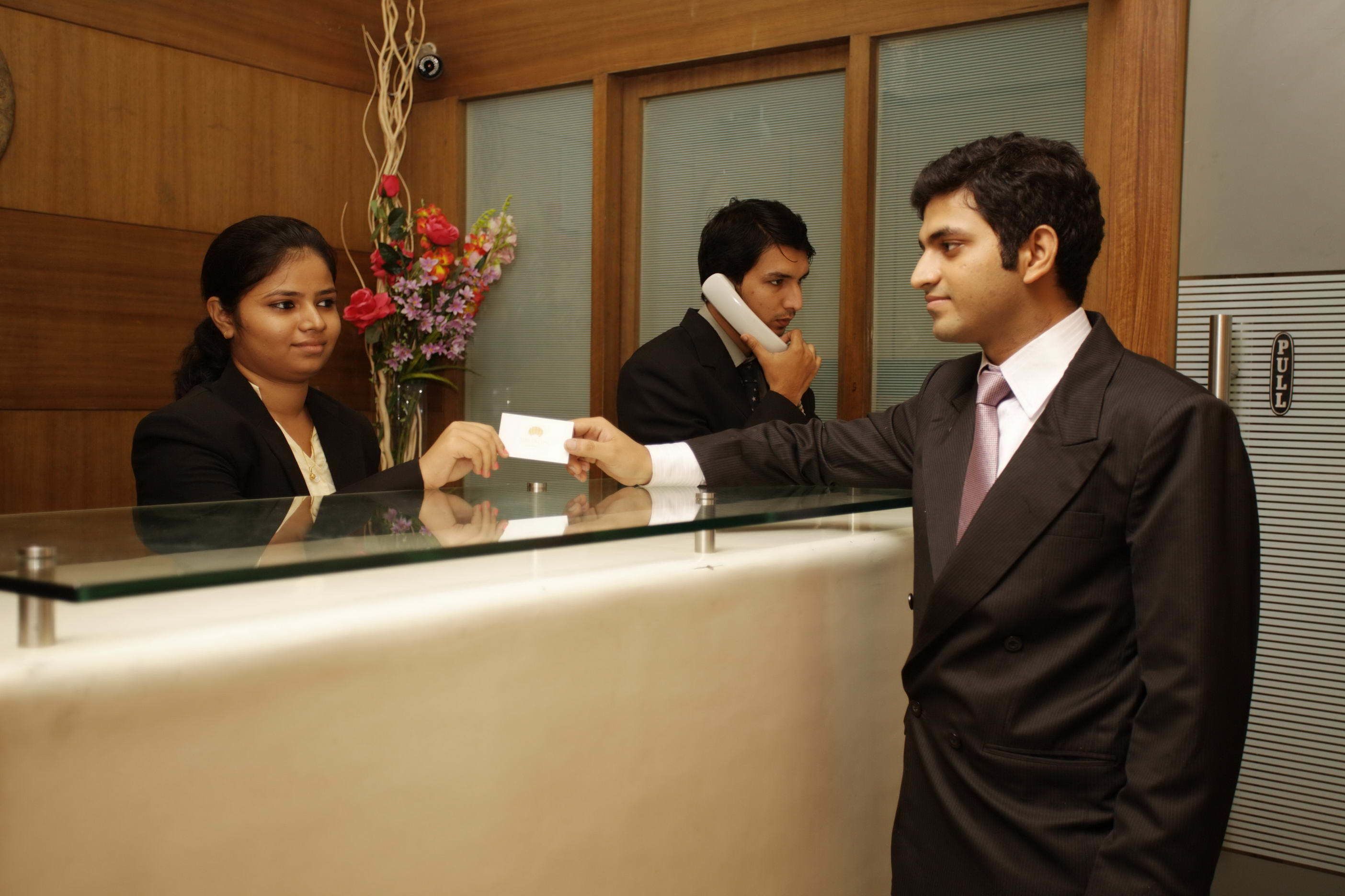 A reception desk with a glass partition, wooden paneling on the walls, and a floral arrangement.