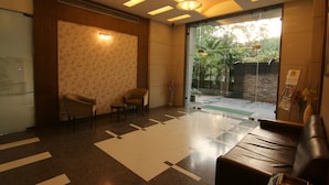 A modern lobby with a reception desk, two chairs, a sofa, and a large glass door leading outside. - The Caliph Hotel (Mumbai)