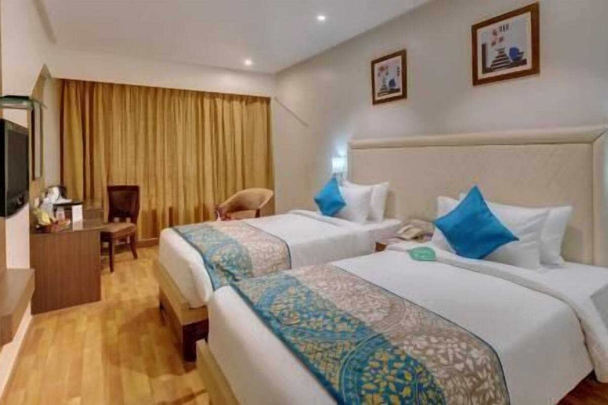 A hotel room with two beds, a desk, a chair, a television, and curtains.