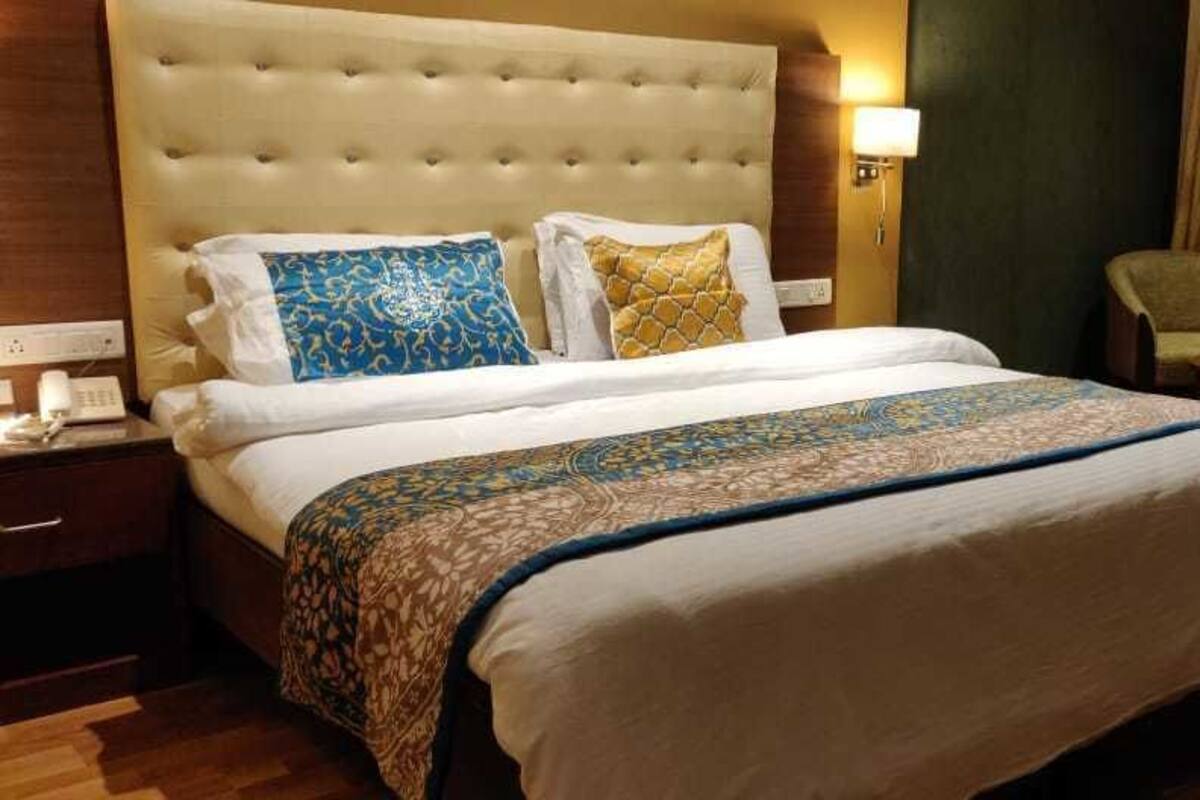 A hotel room with a large bed, a nightstand, a chair, and a window with curtains.
