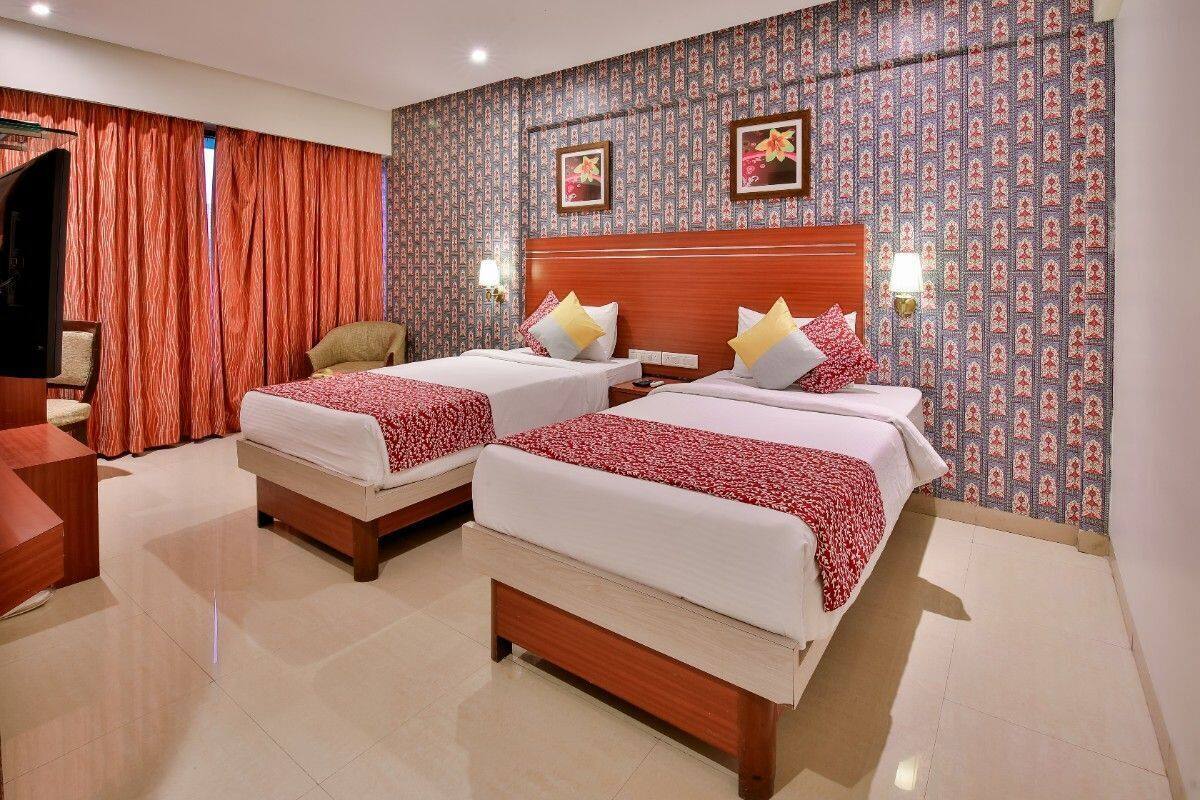 A hotel room with two beds, a wooden headboard, a red and white patterned wall, and a red curtain.