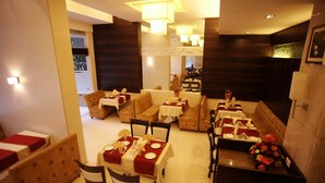 A restaurant with multiple dining areas, including booths and tables, all set with white tablecloths and red napkins. - The Caliph Hotel (Mumbai)
