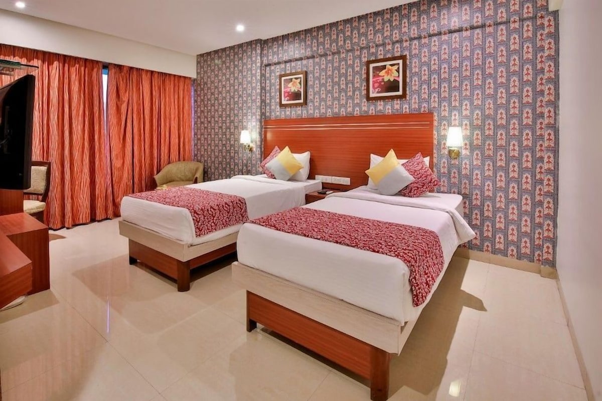 A hotel room with two beds, a desk, a chair, and a large window with curtains.