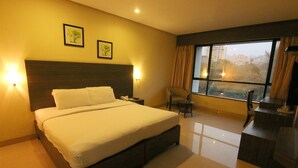 A hotel room with a large bed, a desk, a chair, and a window with a view of buildings. - The Caliph Hotel (Mumbai)