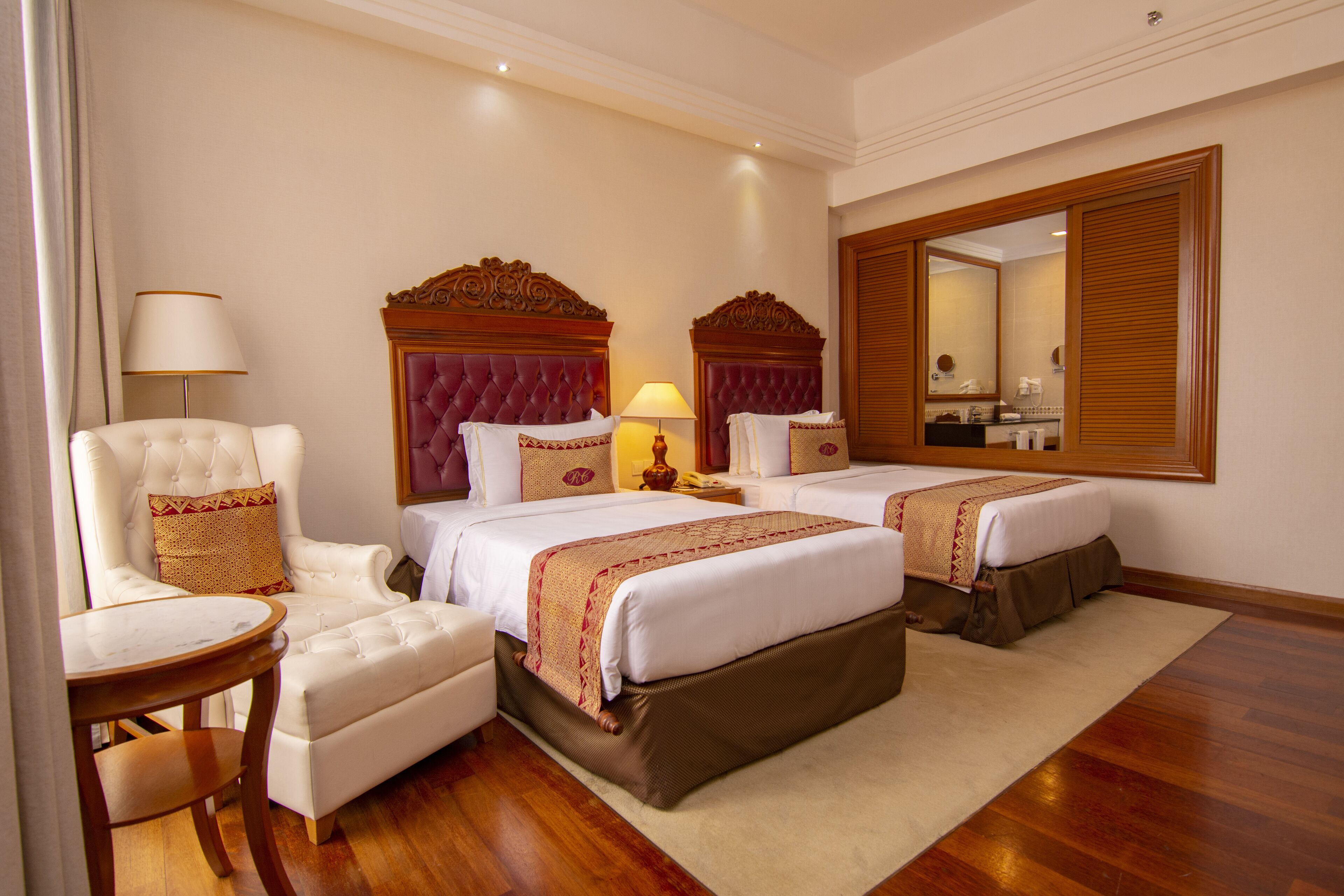 Une chambre d’hôtel avec deux lits, un coin salon comprenant une chaise, une table et un grand miroir.