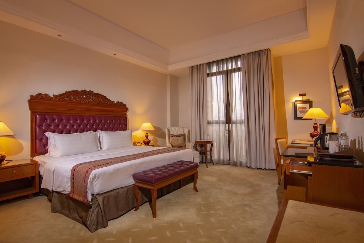 A hotel room with a large bed, a desk, a chair, and a television.
