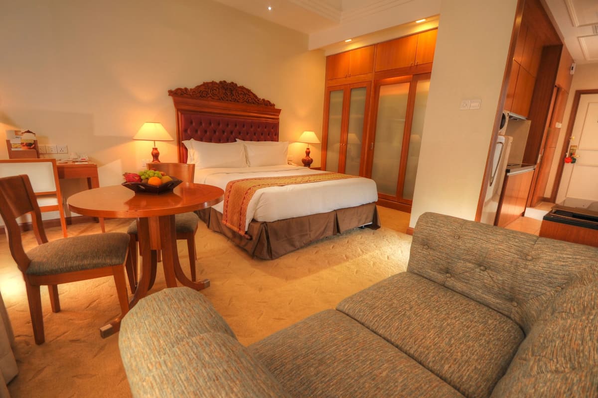 A hotel room with a bed, a dining table with chairs, a sofa, and a fruit bowl.