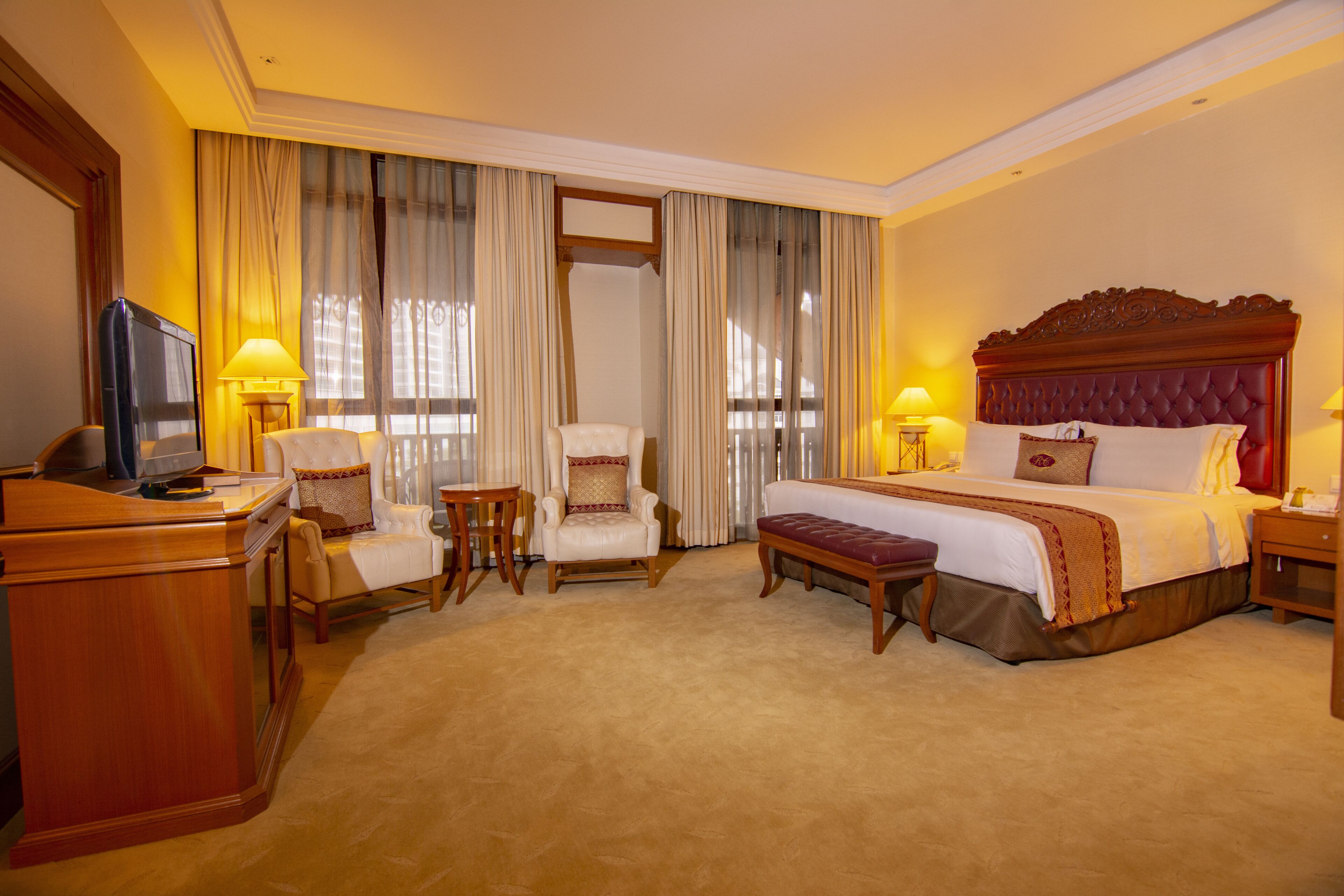A hotel room with a large bed, a desk, a chair, a small table, and a television.