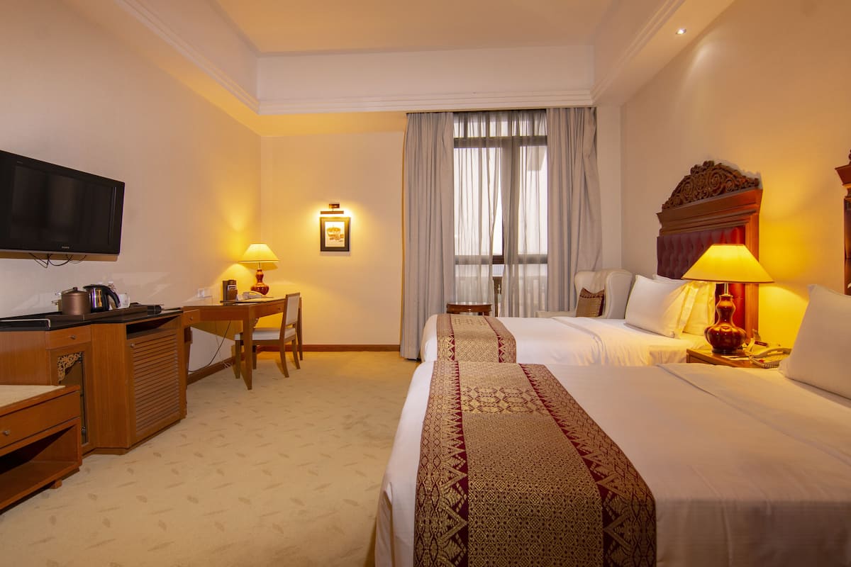 A hotel room with a bed, a desk with a chair, a television, and a window with curtains.