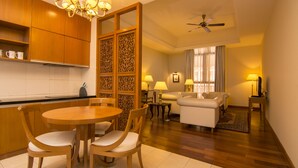 Habitación de hotel con comedor, sala de estar, suelo de madera, ventilador de techo y un separador decorativo.