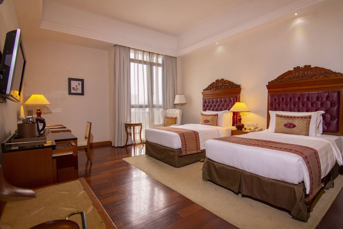 A hotel room with two beds, a desk with a lamp, a chair, and a television.