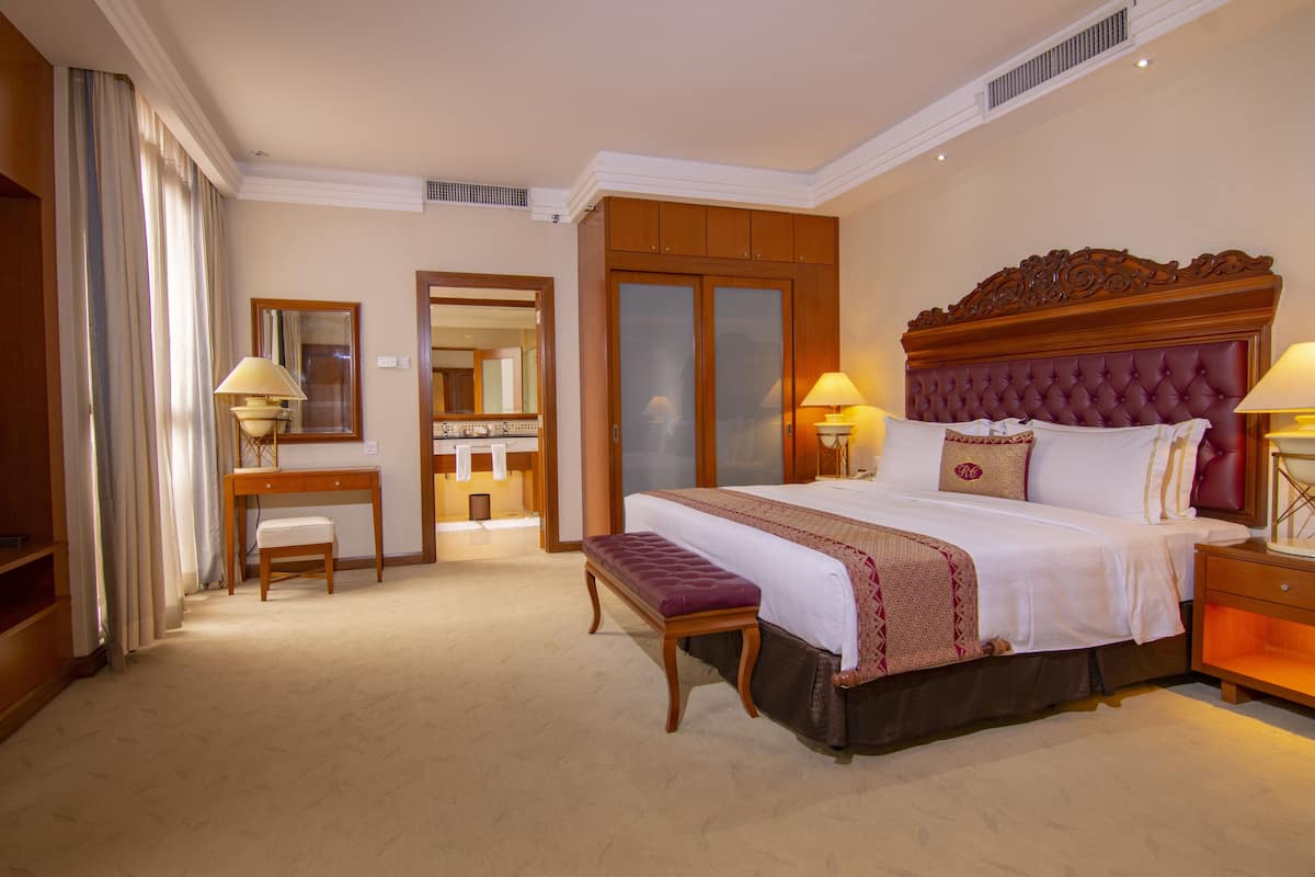 A hotel room with a large bed, bedside tables, a desk, a chair, and a wardrobe.