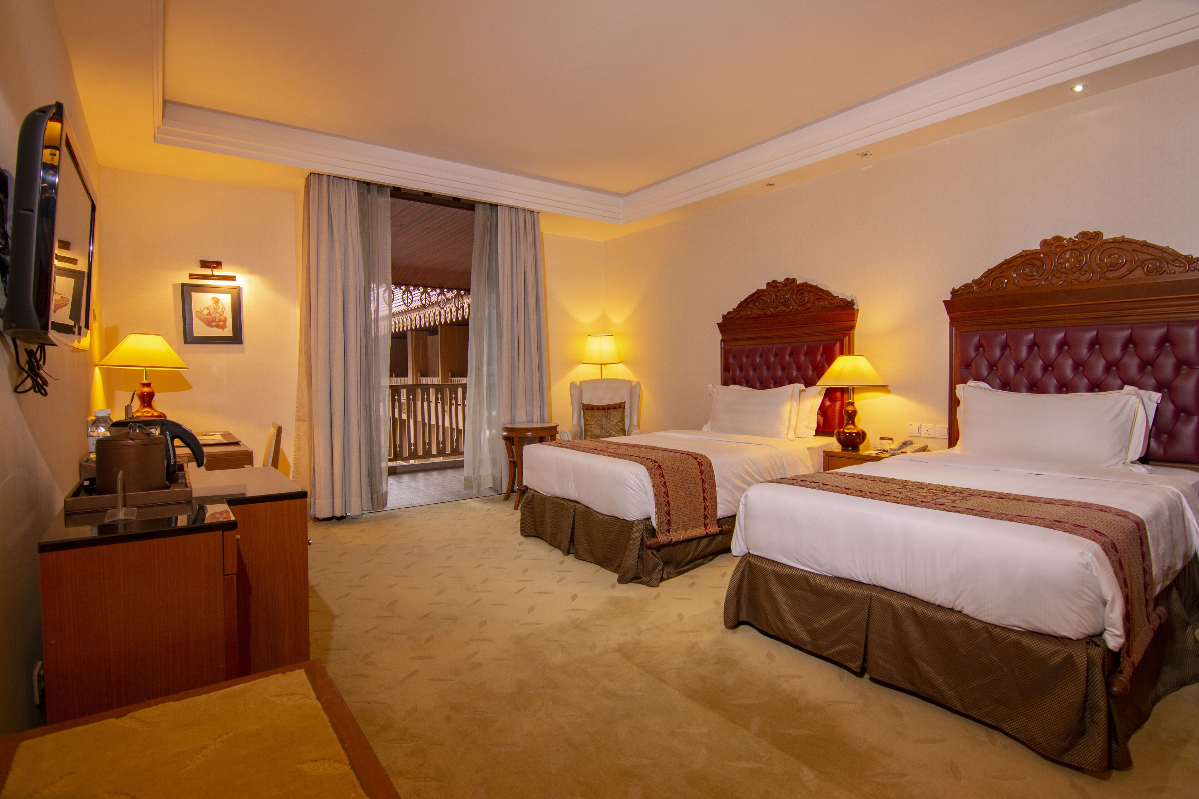 A hotel room with two beds, a desk, a chair, and a television.