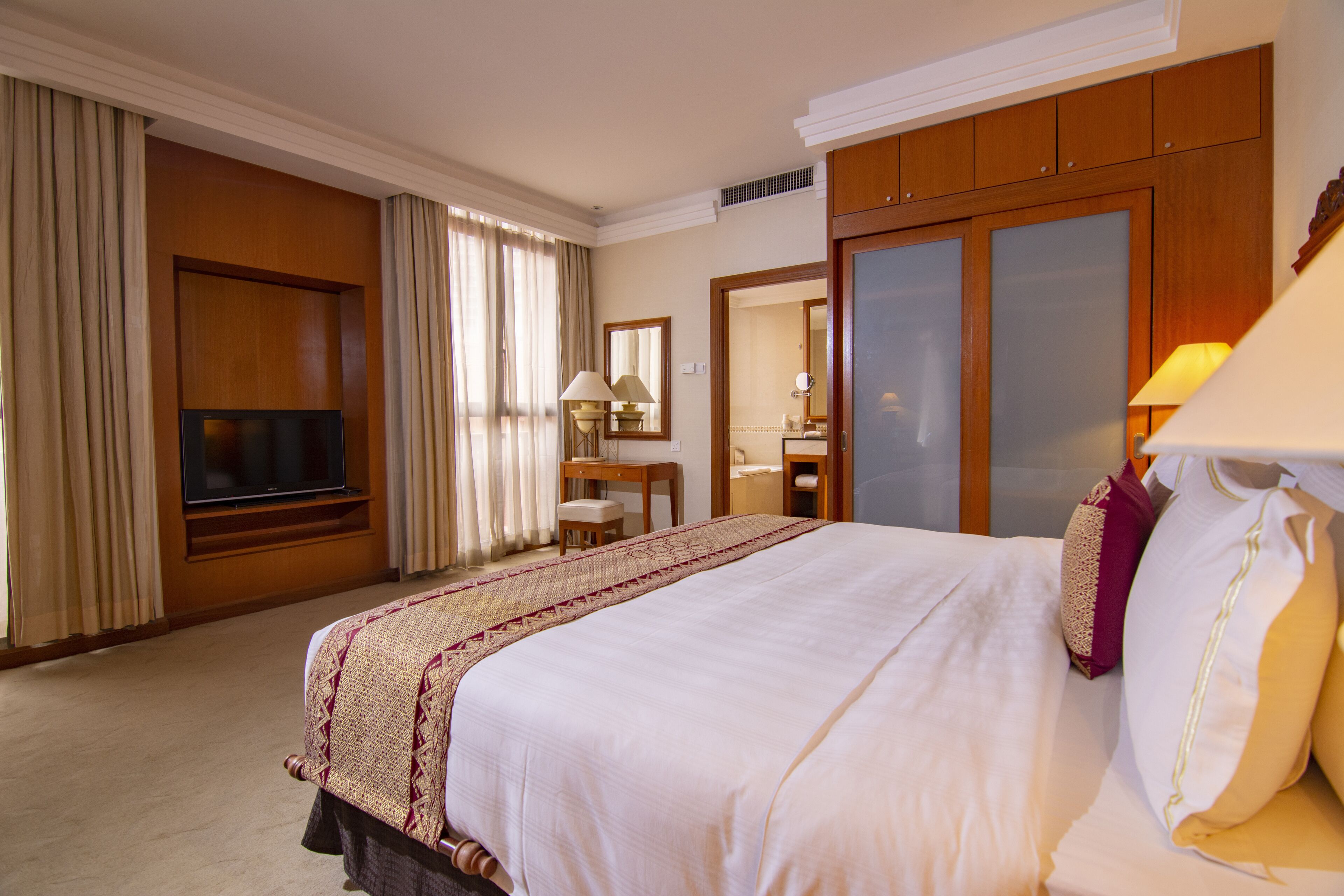 A hotel room with a large bed, a television, a desk with a chair, and a mirror.
