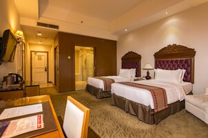 A hotel room with two beds, a sitting area, a desk with a chair, and a bathroom visible through an open door.