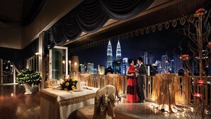 Un restaurante con vistas al horizonte de la ciudad, incluyendo las Torres Petronas, un árbol de Navidad y una mesa dispuesta para dos.