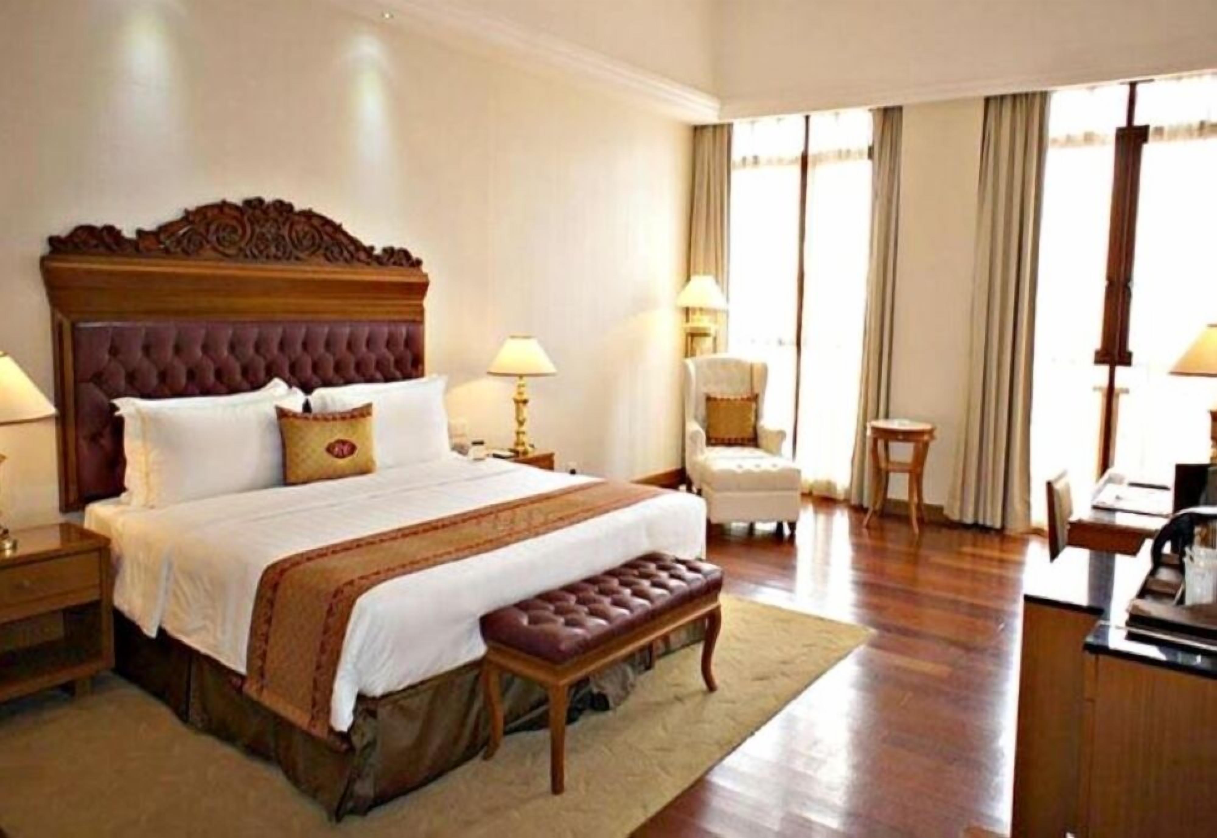 A hotel room with a large bed, a bench, two bedside tables, a chair, and a desk with a lamp.